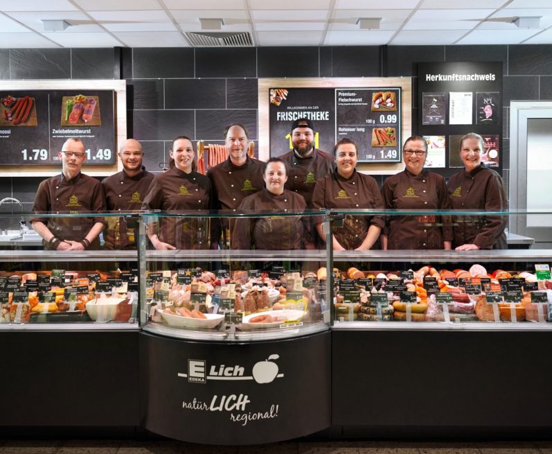 Metzgereiteam Ein Team von Metzgereimitarbeitern steht vor einer Vitrine mit Wurst und anderen Speisen.