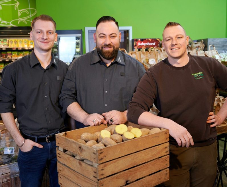 Abteilungsleitung Obst und Gemüse Drei Männer stehen vor einer Kiste mit Kartoffeln in einem Geschäft.